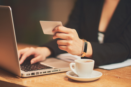 Mixed race woman in coffee shop having coffee and using credit card for paying onlineの写真素材
