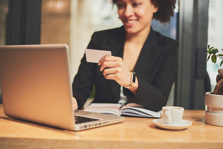 Mixed race woman in coffee shop having coffee and using credit card for paying onlineの写真素材
