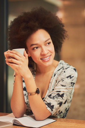 Mixed race business woman taking pause from work and sitting in coffee shop while drinking coffeeの写真素材