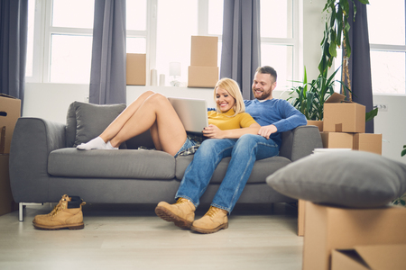 Couple using laptop in new apartment while sitting on sofaの写真素材
