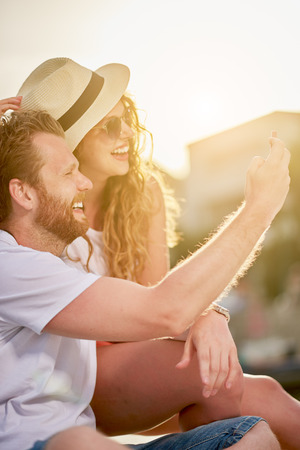 Couple taking selfie while sitting at the beach/ sea in backgroundの写真素材