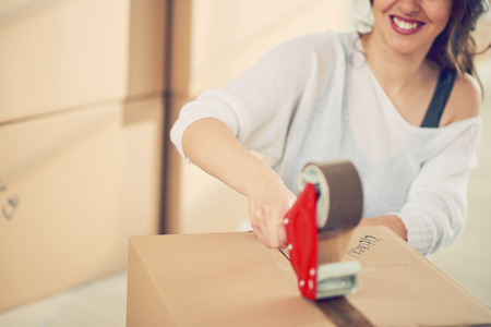 Caucasian girl taping boxes for moving in new apartment