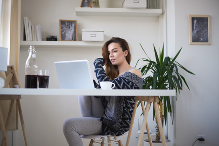 Beautiful Caucasian girl sitting in living room and using laptop in the morningの写真素材