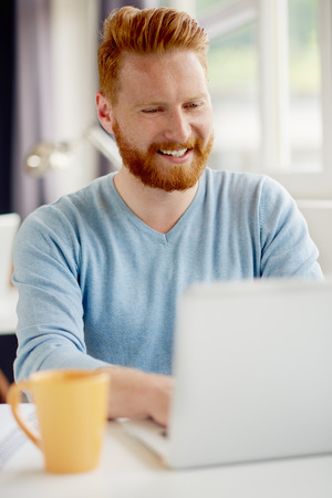 Young Caucasian businessman sitting and using laptop computer in modern office. In background colleagueの写真素材