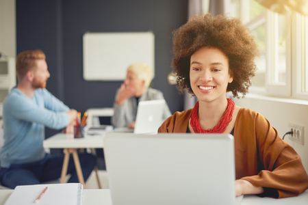 Mixed race businesswoman sitting in modern office and using laptop for sending e mailの写真素材