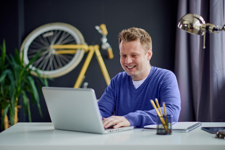 Happy young freelancer using laptop computer for communication with clients while sitting in home...