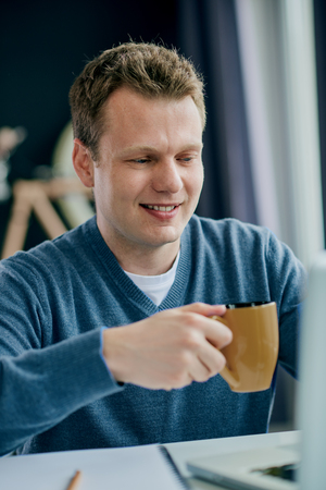 Businessman using laptop and drinking coffee while sitting at home officeの写真素材