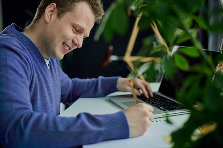 Businessman taking notes and using laptop while sitting at home office