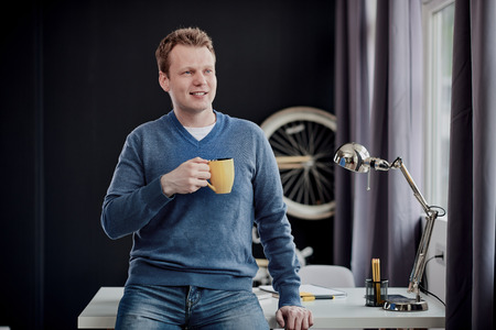 Businessman standing against the desk and drinking coffeeの写真素材