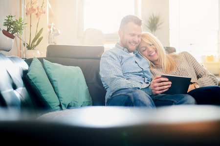 Caucasian couple using tablet while sitting on sofa in living roomの写真素材