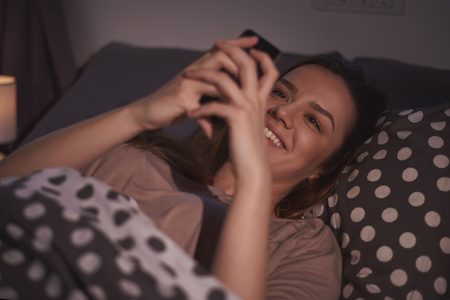 Beautiful Caucasian girl using smart phone in bed late at night/ internet addiction conceptの写真素材