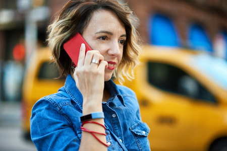 Woman using smart phone in New York City, Manhattan walking, smiling and laughing with yellow cab in background.の写真素材