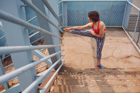 Beautiful young woman in sporty outfit doing some stretching exercises before going for a run in the...