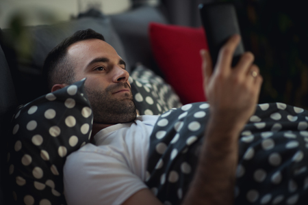 Man chatting over the smart phone while lying in bed, internet and social addictionの写真素材