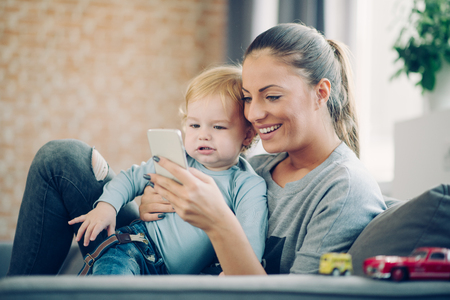 Mom and toddler taking selfie in cosy living roomの写真素材
