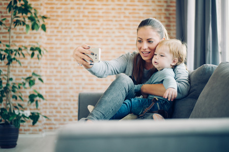 Mom and toddler taking selfie in cosy living roomの写真素材