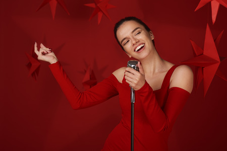 Girl singing and holding microphone. Red background and stars behindの写真素材