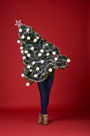 Girl standing and holding christmas tree. Red background. Christmas conceptの写真素材