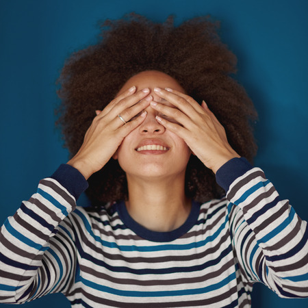 lose up of mixed race woman holding hands on eyes. Blue wall in backgroundの写真素材