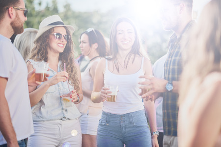 Group of friends talking and drinking while standing at outdoor partyの写真素材