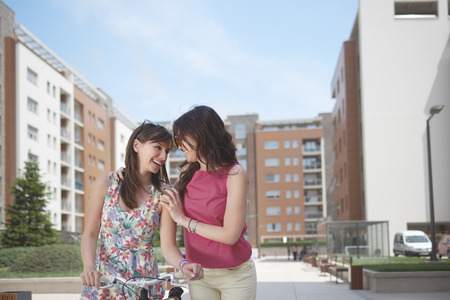 Two girls taking a walk. One girls holding a bicycle and the other embracingの写真素材