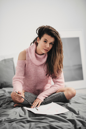 Girl sitting in her bed and paint a painting at the morningの写真素材