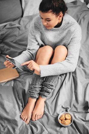 Girl sitting on bed in morning and using tabletの写真素材
