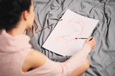 Girl painting with wather color and sitting on the bed in the morningの写真素材