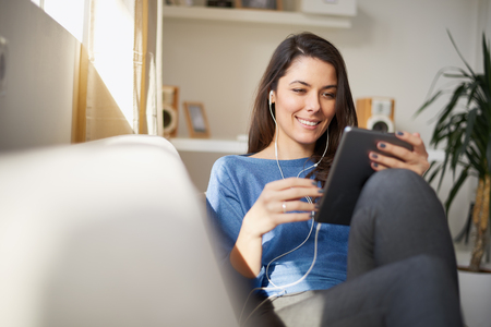 Woman sitting on sofa in living room and using tabletの写真素材