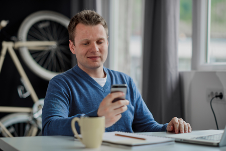 Businessman sitting in modern home office and using smart phone for communication.