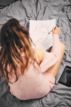 Girl painting with wather color and sitting on the bed in the morningの写真素材