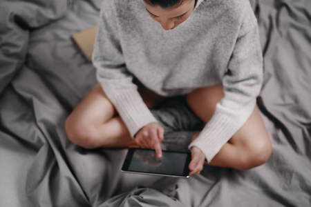Girl sitting on bed in the morning and using tablet for reading newsの写真素材