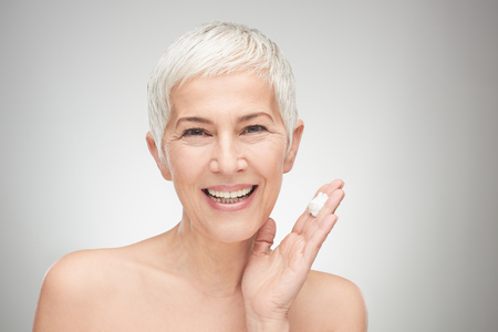 Head shot of beautiful senior woman putting on the creme.の写真素材