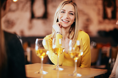 Portrait of young beautiful blonde woman in the bar. Glasses of wine in front of her.の写真素材