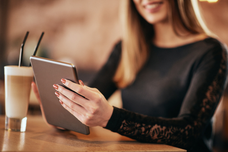 Close up of woman`s hands holding tablet. Cafe interior.の写真素材