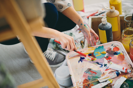 Close up of girl`s hands holding paint brush and mixing colors for painting.の写真素材
