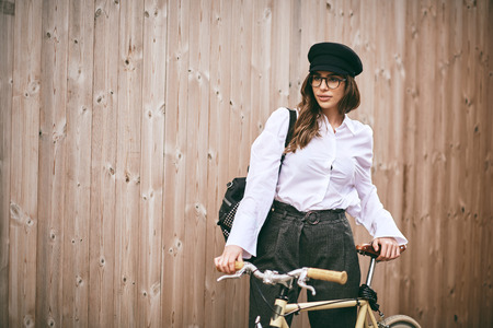 Portrait of beautiful brunette holding bicycle. Wooden background.の写真素材