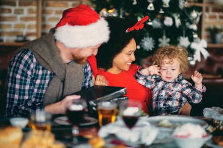 Man and mixed race woman giving toddler  Christmas gift while sitting at table. Christmas holidays concept.の写真素材