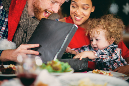 Man and mixed race woman giving toddler  Christmas gift while sitting at table. Christmas holidays concept.の写真素材