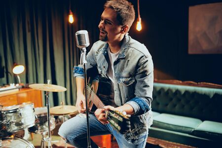 Talented bearded Caucasian musician playing acoustic guitar and singing at home studio.の写真素材