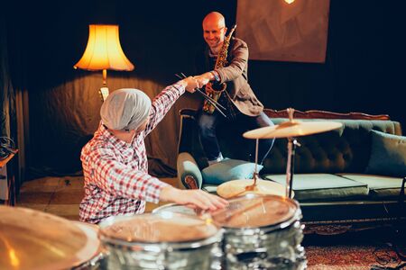 Musicians giving fist bump. On picture saxophonist and drummer sitting in home studio.