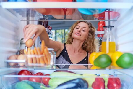 Young Caucasian woman taking egg from fridge to make a breakfast. Picture taken from inside of fridge.の写真素材