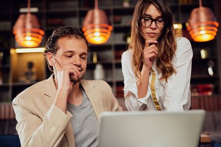 Two colleagues dressed smart casual looking at laptop and trying to solve a problem. Cafe interior.