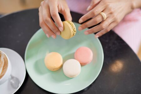 Top view of mixed race woman in pink striped dress holding cookie while sitting in pastry shop. On table are coffee and plate with cookies.の写真素材