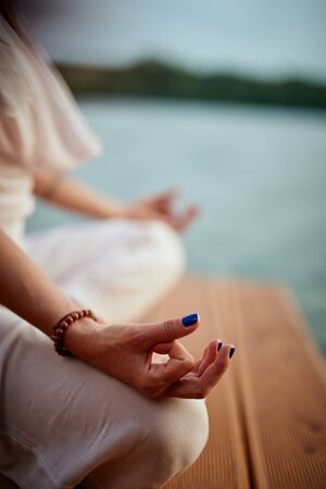 Close up of woman dressed in white meditating near river.の写真素材