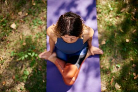 Top view of beautiful Cucasian brunette dressed in sports clothing sitting on mat in nature in knee pile yoga pose.の写真素材