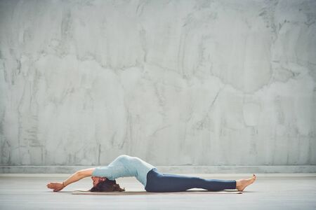 Full length of beautiful Caucasian brunette lying down on mat with hands outstretched and doing fish yoga exercise.の写真素材