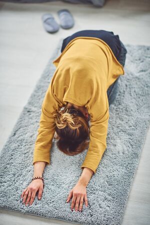 Brunette doing Extended Child's yoga posture on the rug in bedroom.