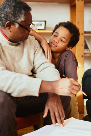 An African-American grandfather is sitting at home with his grandson and explaining a math problem...