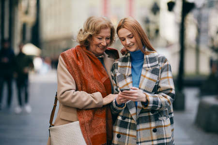 A grandmother and her grandchild standing on the street and reading messages on the phone.の写真素材